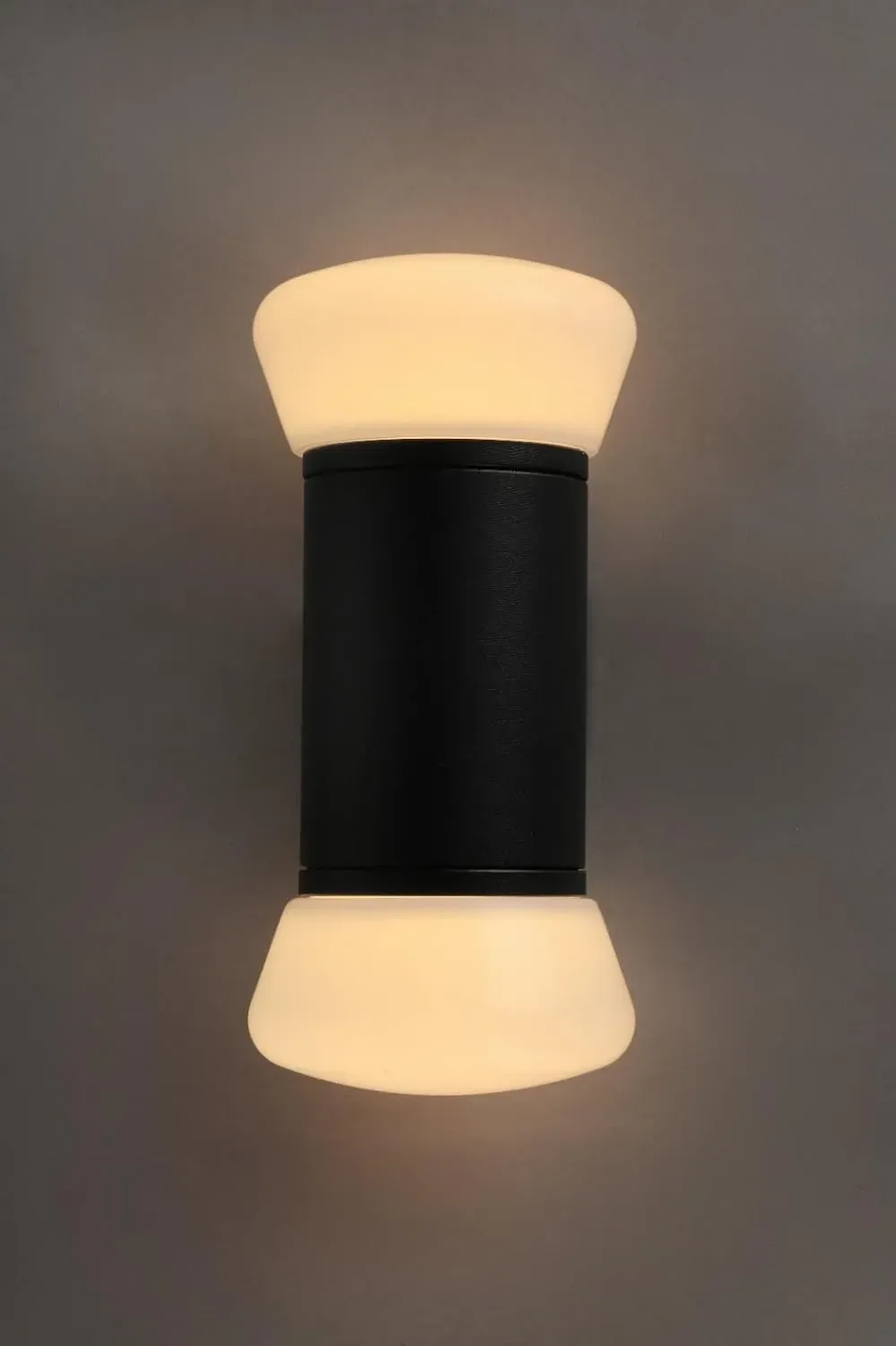 Black up down outdoor wall light with opal drum shades, lit warm white against a dark background