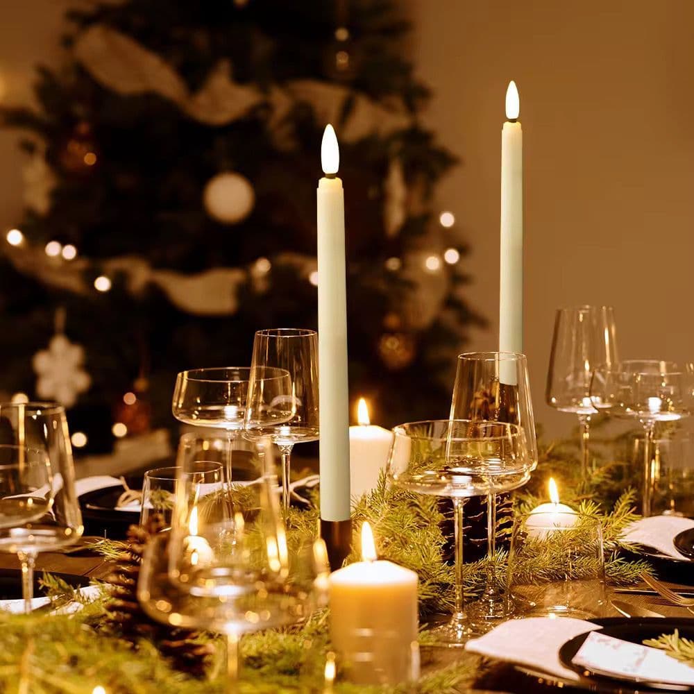 Flameless taper candles lit on a festive table setting beside a Christmas tree