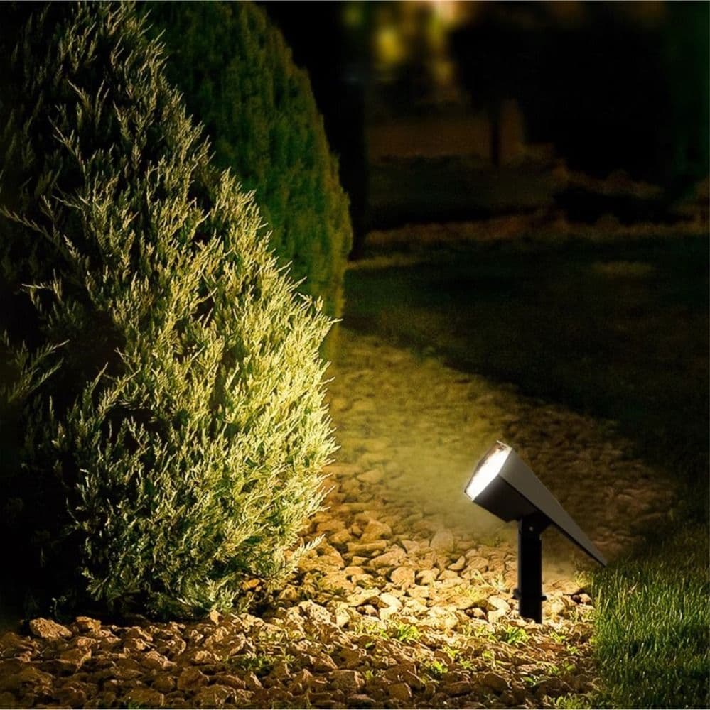 Solar spike spotlight lit warm, uplighting shrubs in a garden path at night