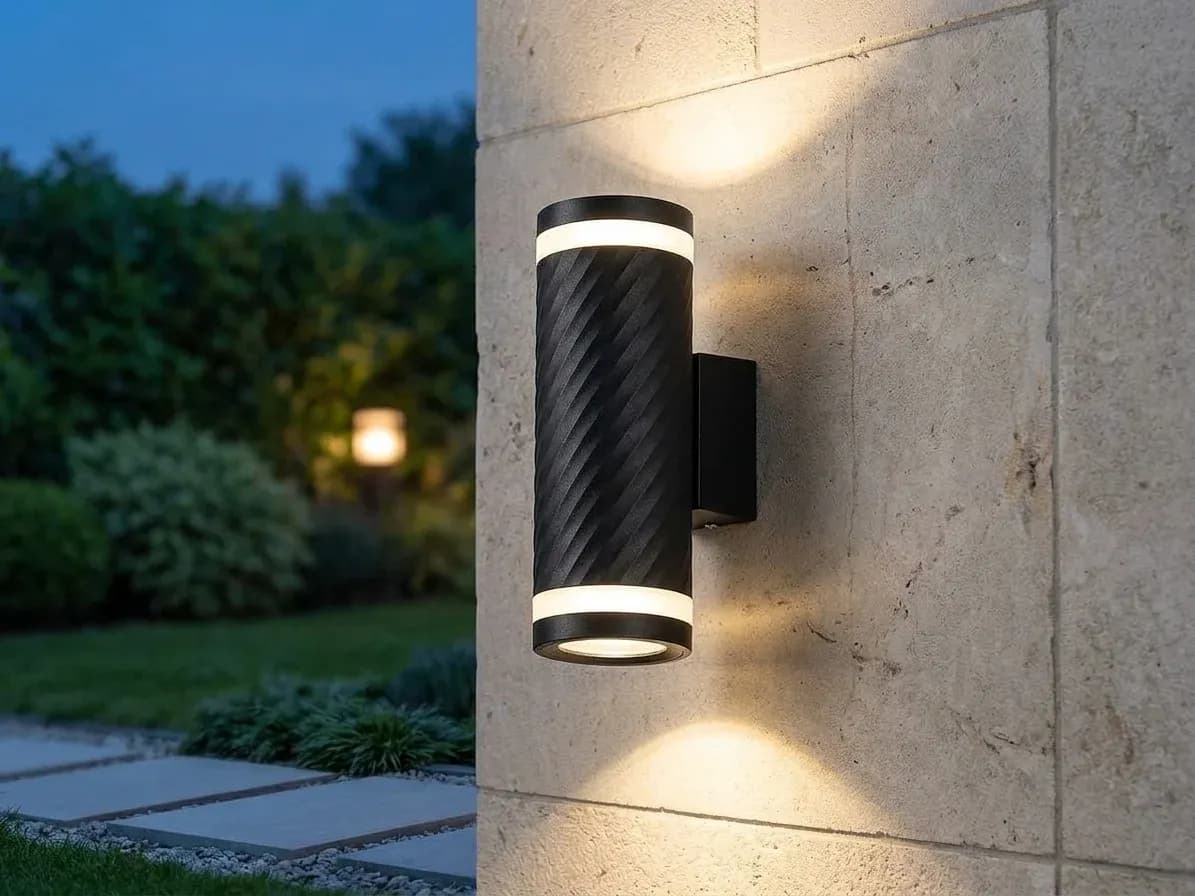 Black up and down outdoor wall light lit on an exterior wall at dusk